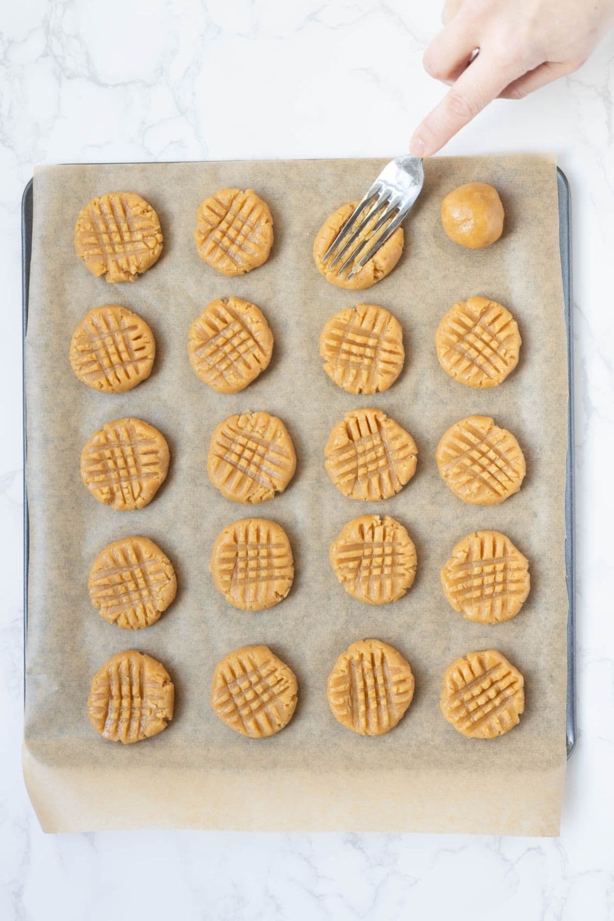 Peanut butter cookie dough balls pressed with a fork on a parchment-lined baking sheet before baking.