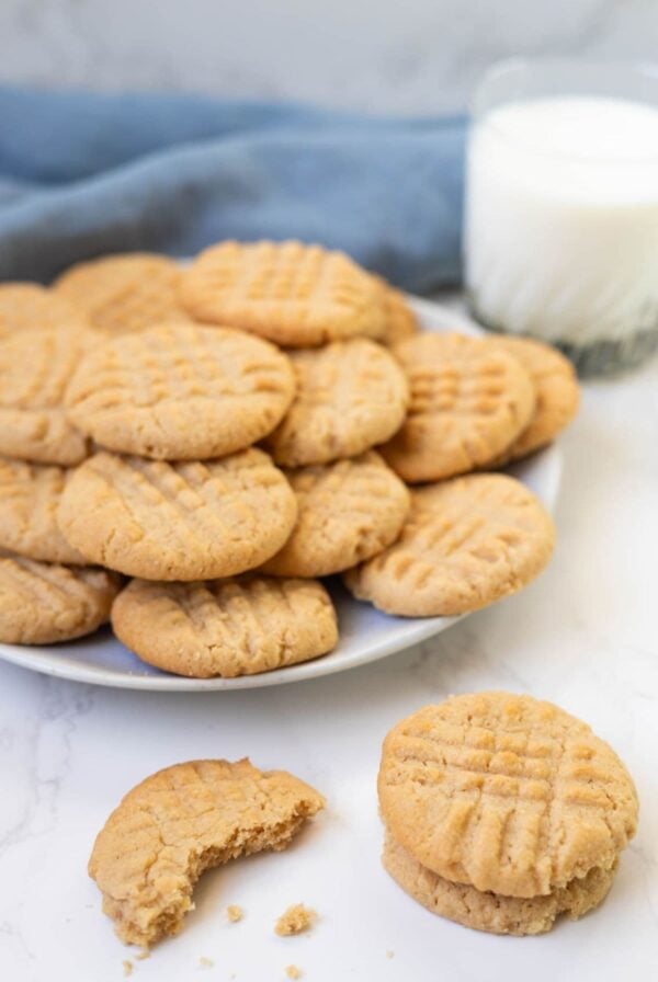 Plate of soft sourdough peanut butter cookies served with milk and a bitten cookie in the foreground.