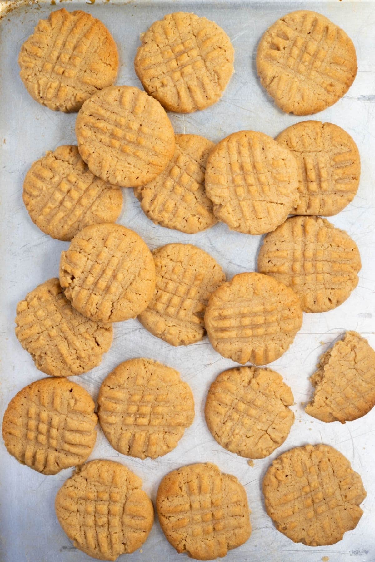 Freshly baked sourdough peanut butter cookies cooling on a baking sheet with one cookie partially eaten.