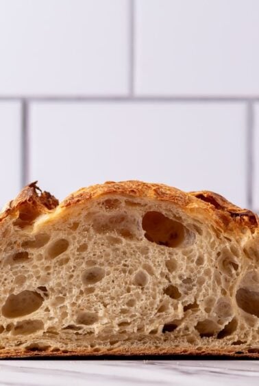 A photo taken front on of a loaf of sourdough bread sliced open through the middle so you can see the crumb inside.
