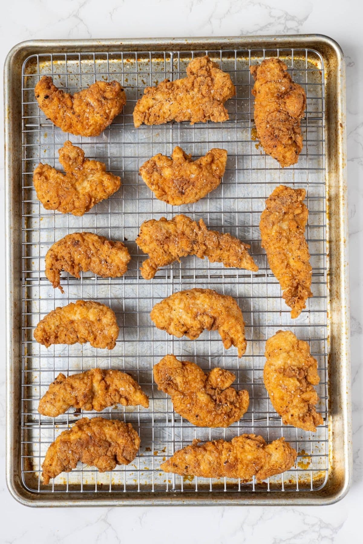 Freshly fried sourdough chicken tenders cooling on a wire rack after frying.
