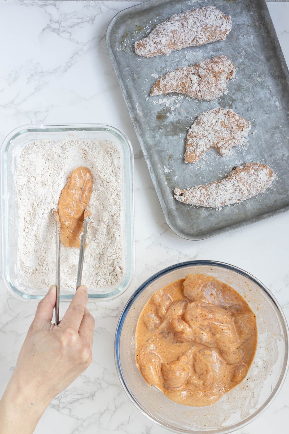 Marinated chicken tender being coated in seasoned flour before frying for sourdough fried chicken.