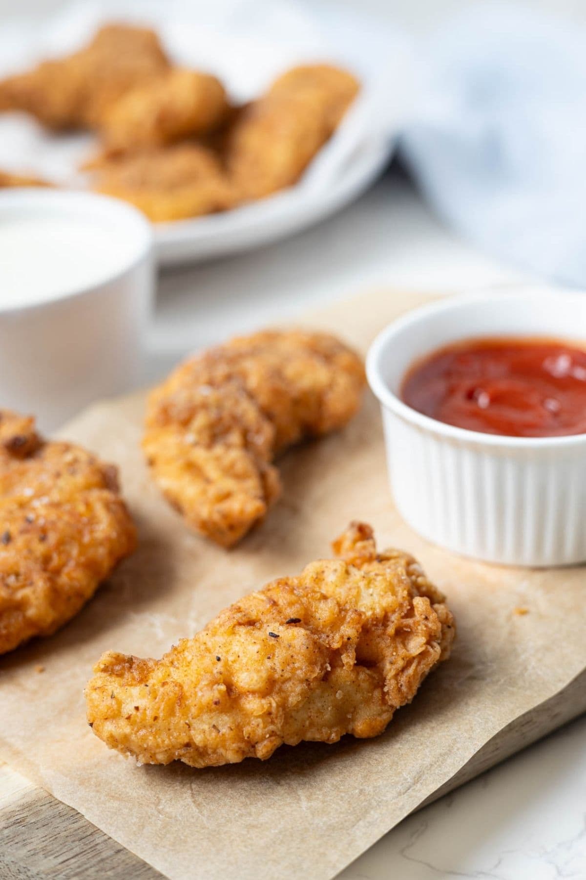 Crispy sourdough fried chicken fingers served on parchment paper with a side of ketchup for dipping.