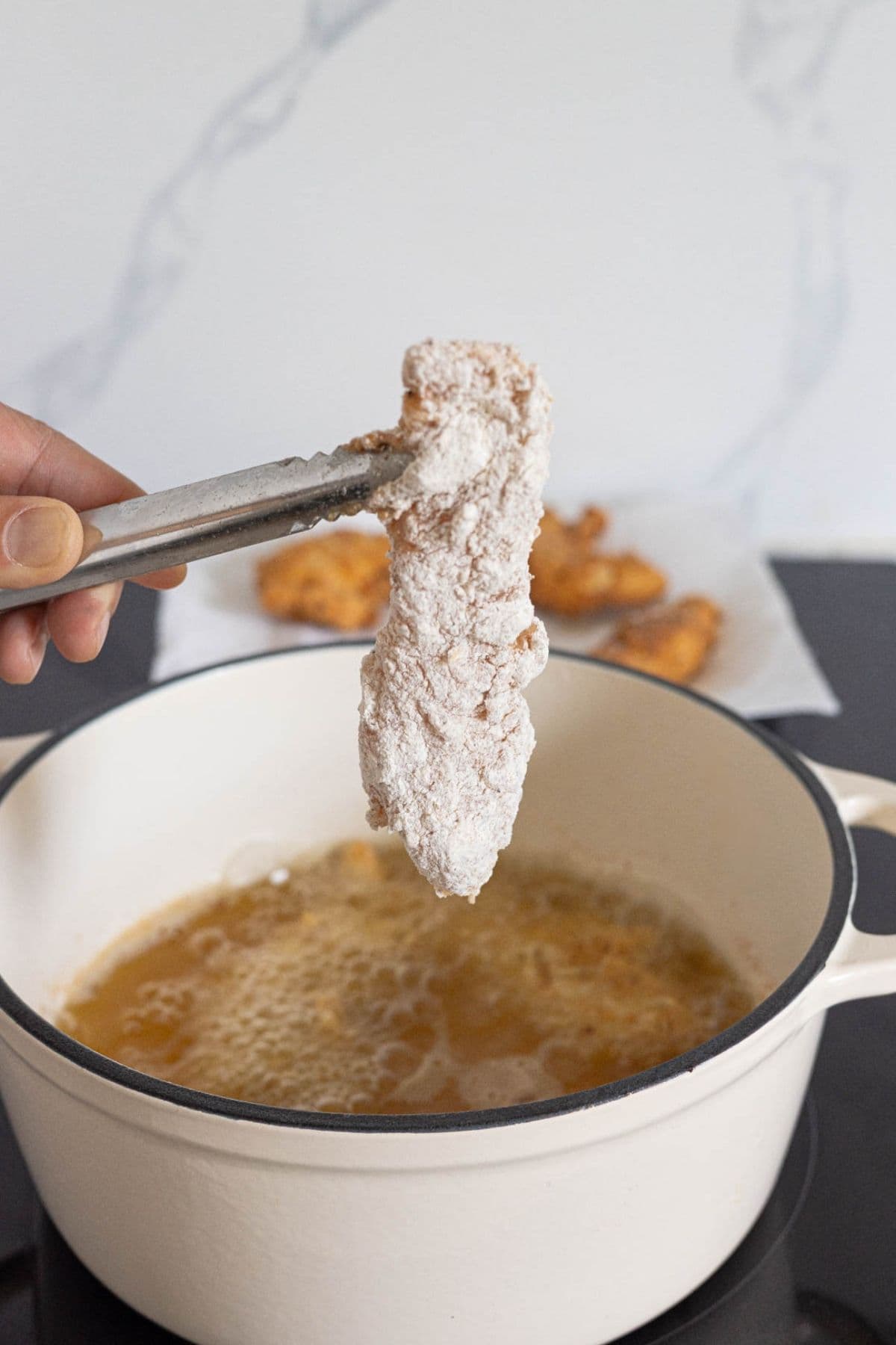 Breaded sourdough fried chicken tender being lowered into hot oil for frying.
