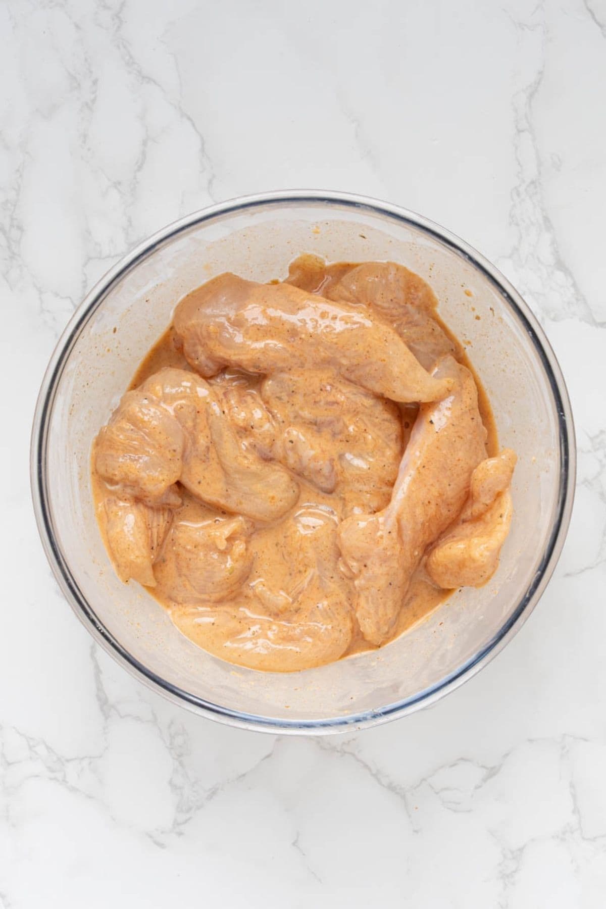 Raw chicken tenders coated in seasoned sourdough discard marinade before frying.