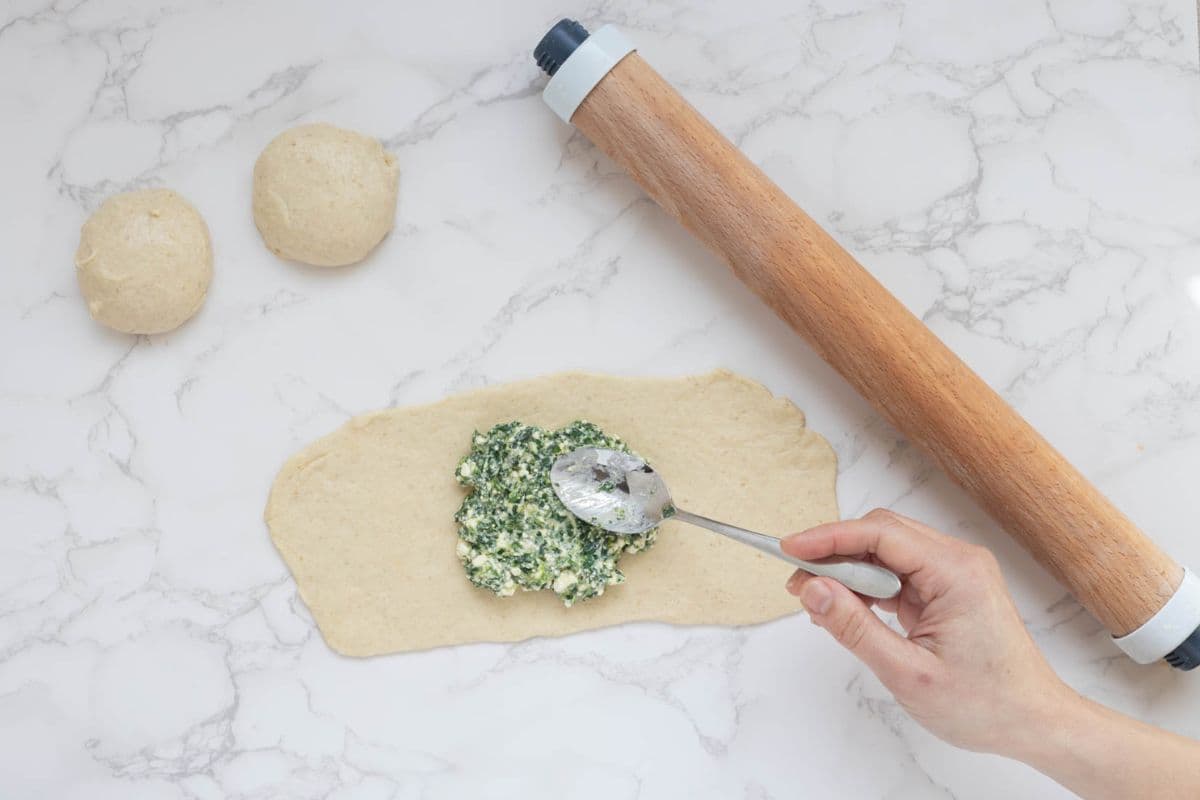 Spinach and feta filling being spooned onto rolled sourdough gozleme dough.