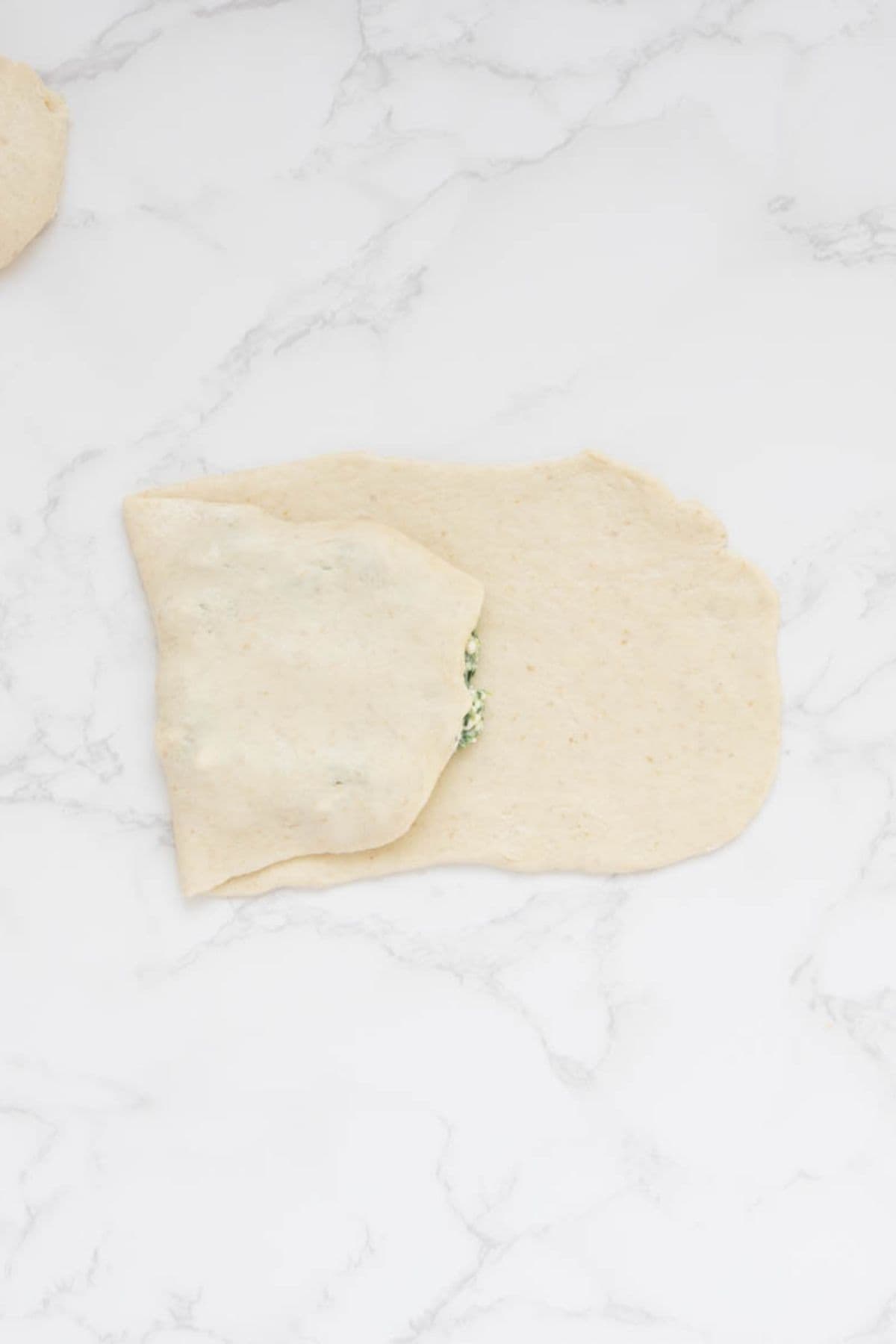 Rolled sourdough dough stretched over spinach and feta filling to form gozleme.