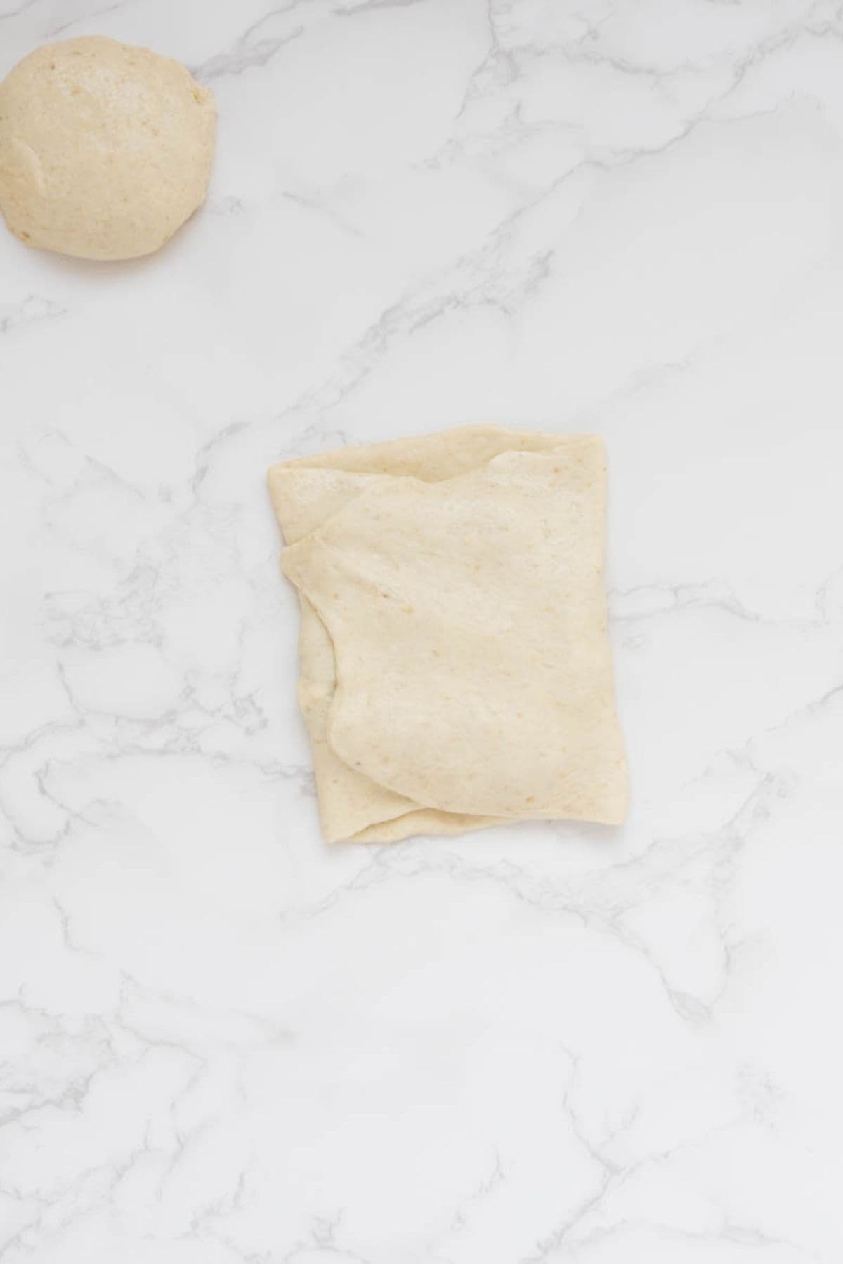 Sourdough gozleme dough folded over spinach and feta filling before sealing.