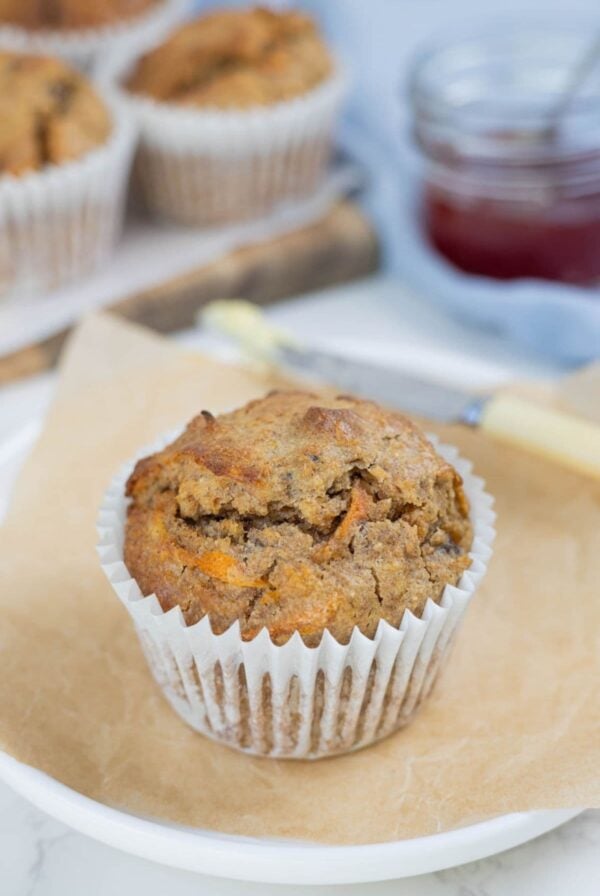 Golden brown sourdough morning glory muffin on a plate with butter, jam and additional muffins in the background.
