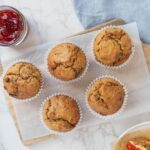 Freshly baked sourdough morning glory muffins arranged on a wooden board beside a jar of jam.