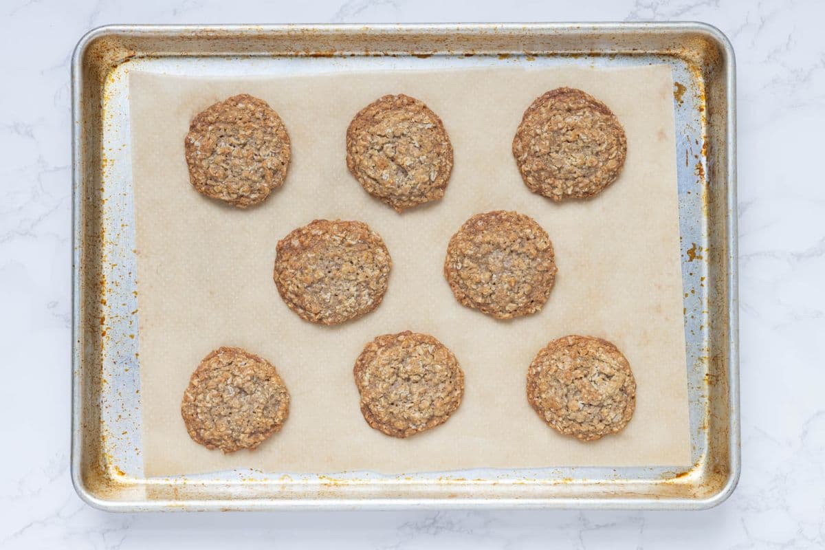 Freshly baked oatmeal cookies cooling on a parchment-lined baking sheet.