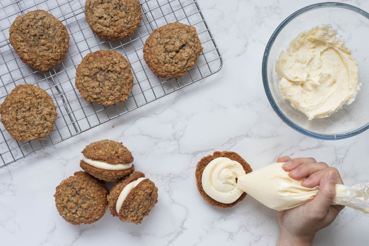 Hand piping vanilla filling onto an oatmeal cookie while assembling sourdough oatmeal cream pies.