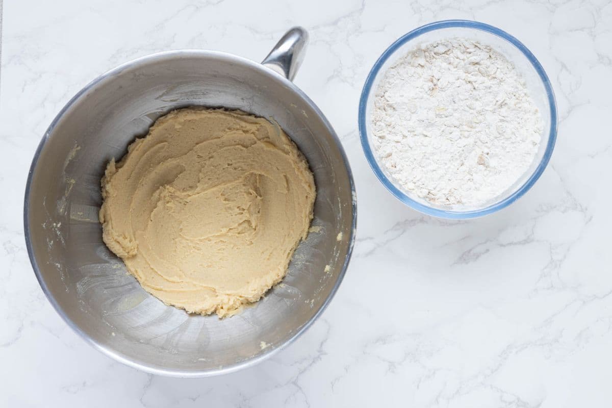 Mixing bowl of creamed butter and sugar beside a bowl of dry ingredients before making oatmeal cookies.