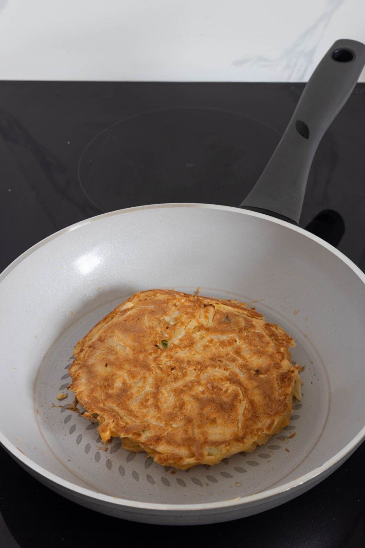 Golden brown sourdough okonomiyaki cooking after being flipped in a skillet.