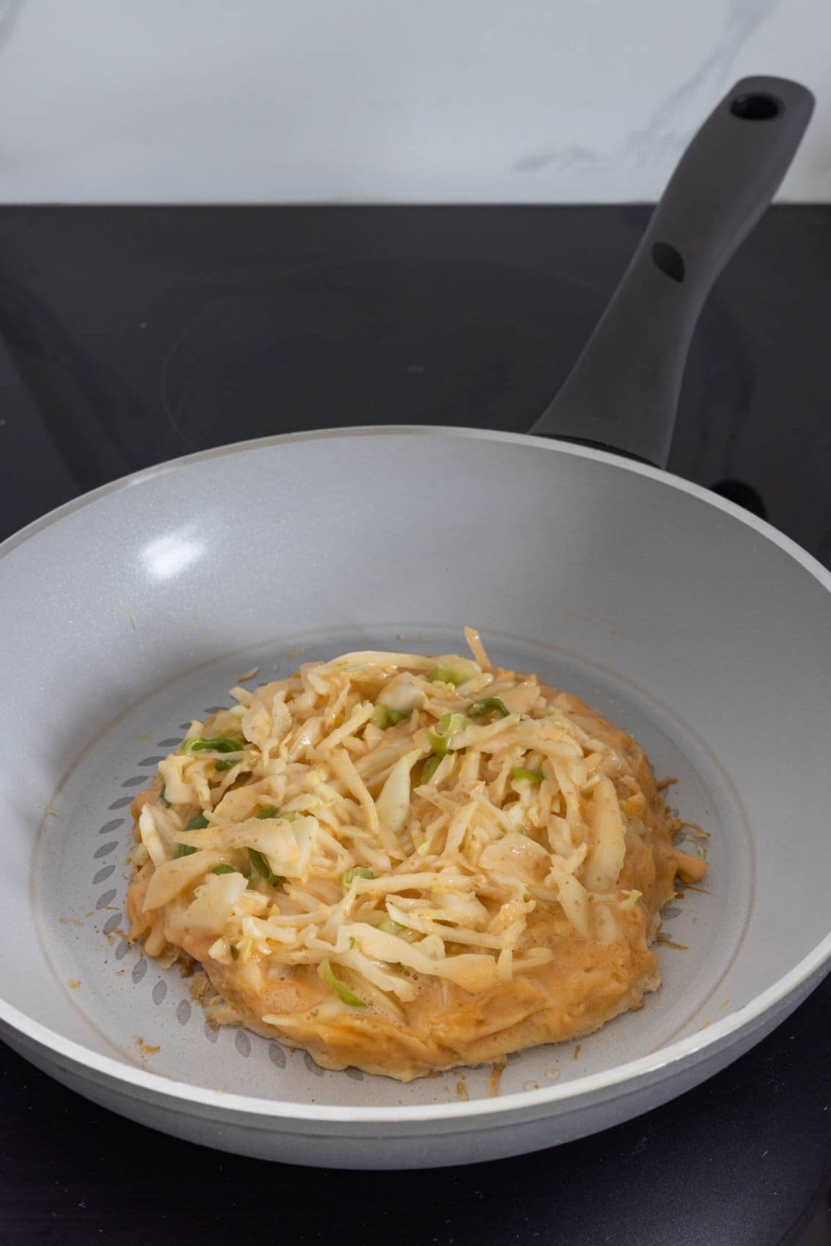 Sourdough okonomiyaki batter with cabbage and scallions cooking in a skillet.