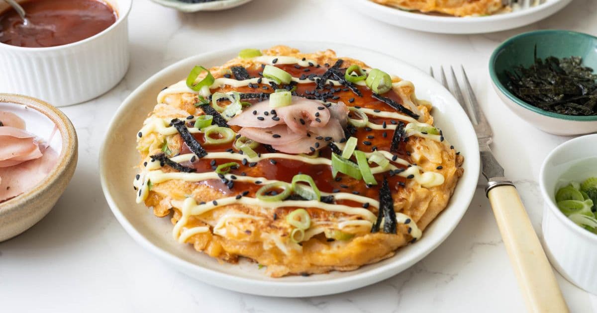 Sourdough okonomiyaki savory Japanese pancake topped with okonomiyaki sauce, mayonnaise, pickled ginger, nori, sesame seeds, and scallions.