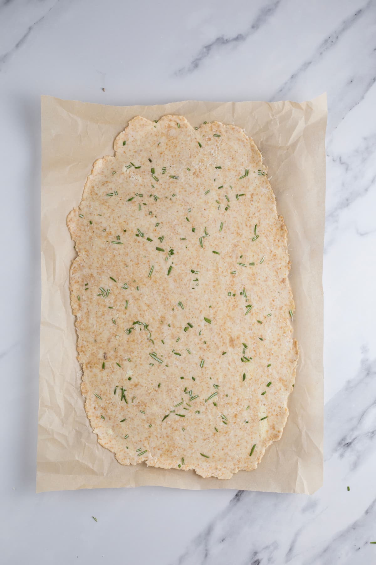 Rolled sourdough cracker dough including chopped rosemary before scoring and baking.
