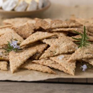 Close up of homemade sourdough parmesan rosemary crackers being served with a plate of cheese.