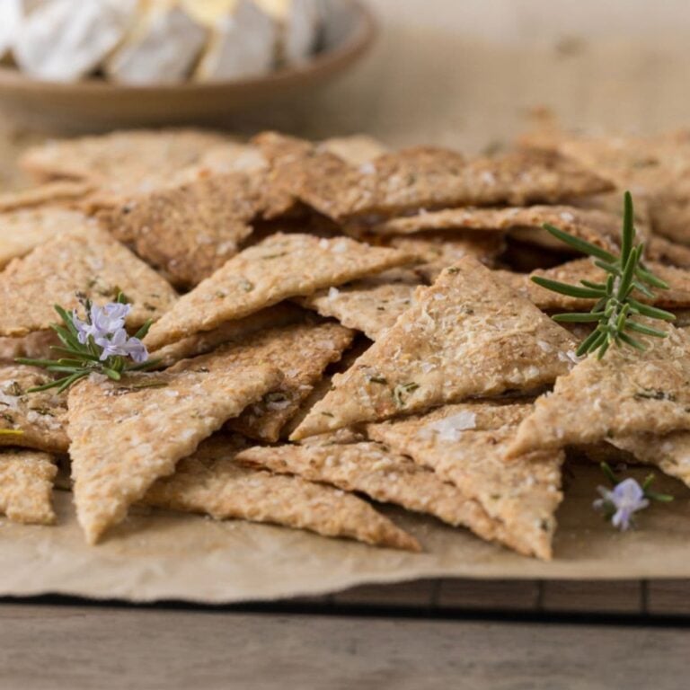 Close up of homemade sourdough parmesan rosemary crackers being served with a plate of cheese.