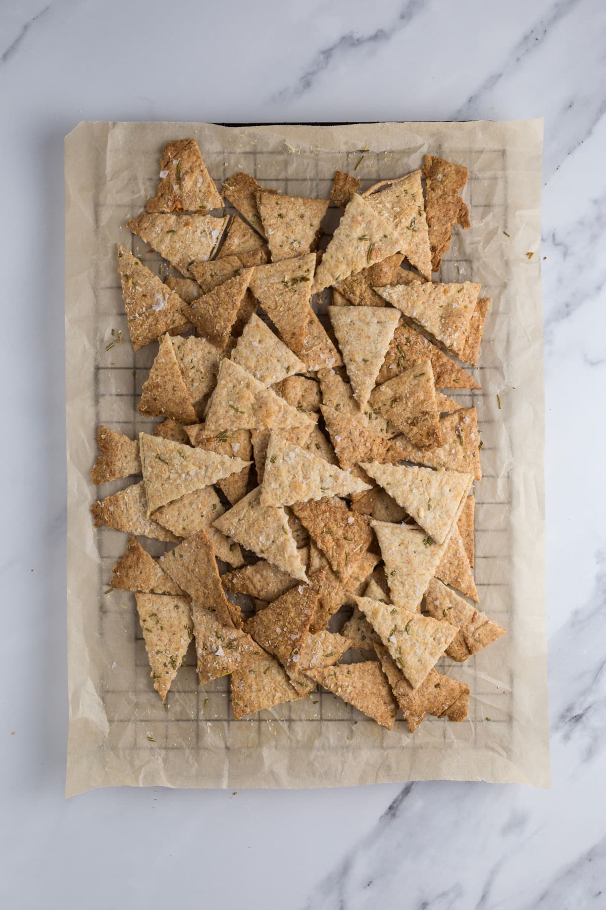 Sourdough parmesan rosemary crackers cooling on a piece of parchment paper over a wire rack.