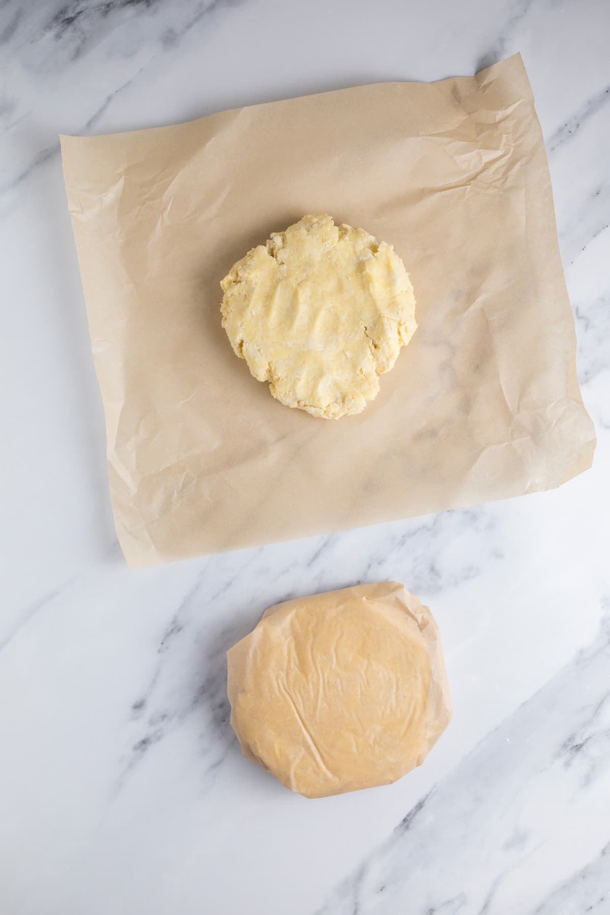 2 discs of sourdough pie crust dough with one wrapped in parchment paper and flattened into a disc for refrigeration and the other ready to be wrapped.