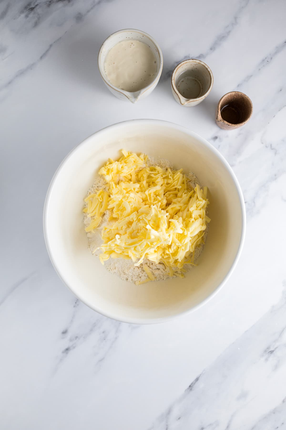 Grated cold butter added to flour in a mixing bowl for making flaky sourdough pie crust dough.