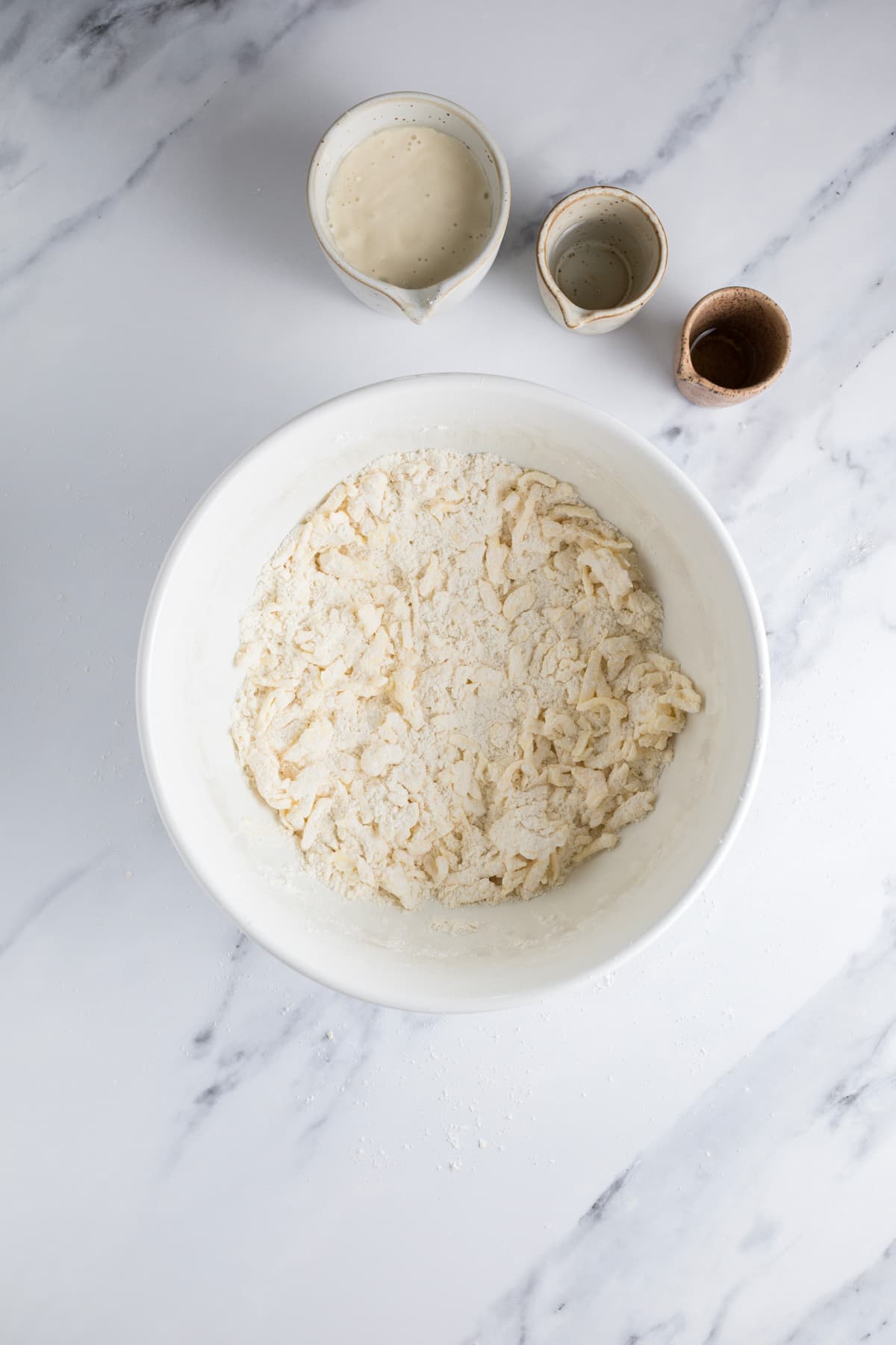 Flour and grated butter combined in a bowl before adding sourdough starter to the pie crust mixture.