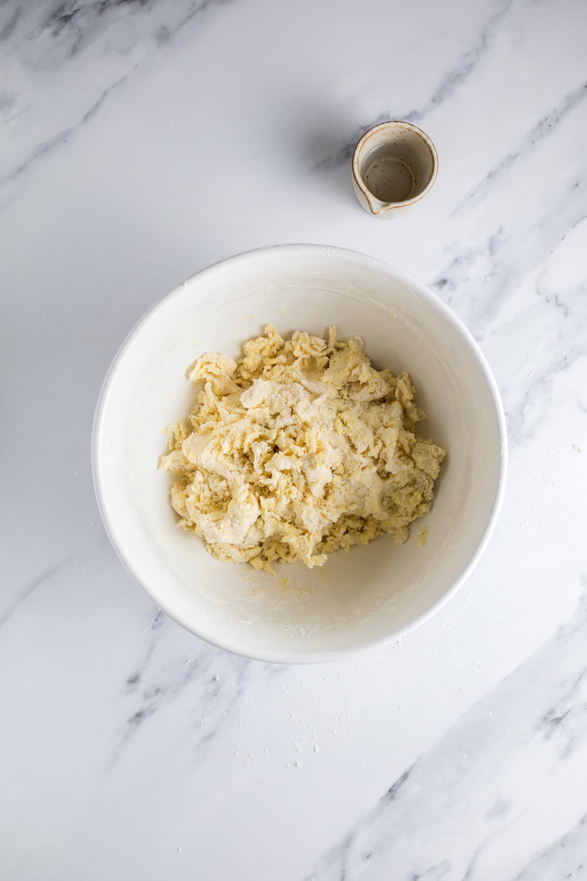 Shaggy sourdough pie crust dough in a mixing bowl before being kneaded together by hand.