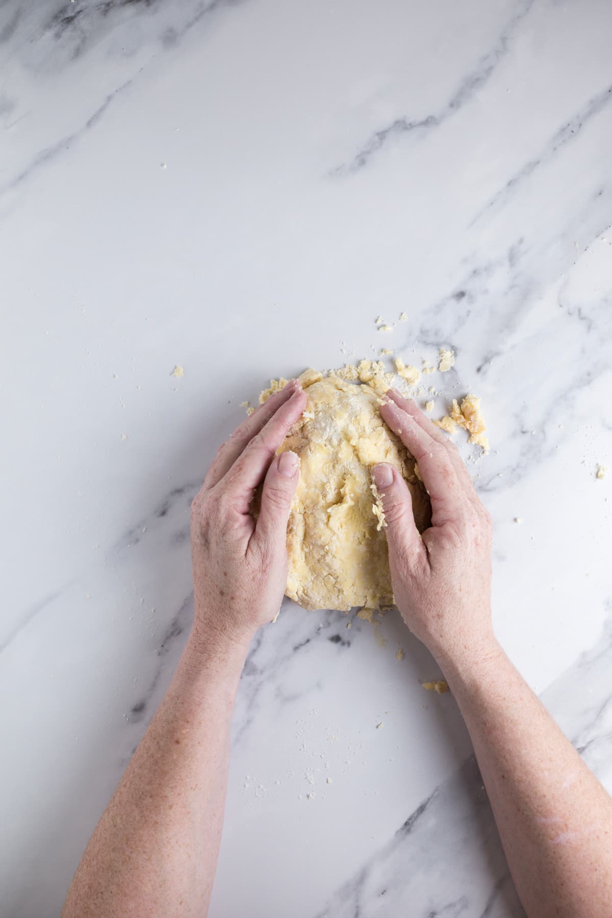 Hands gently pressing crumbly sourdough pie crust dough together into a cohesive ball.