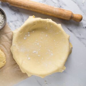 Rolled sourdough pie crust fitted into a pie dish with extra dough and flour nearby.