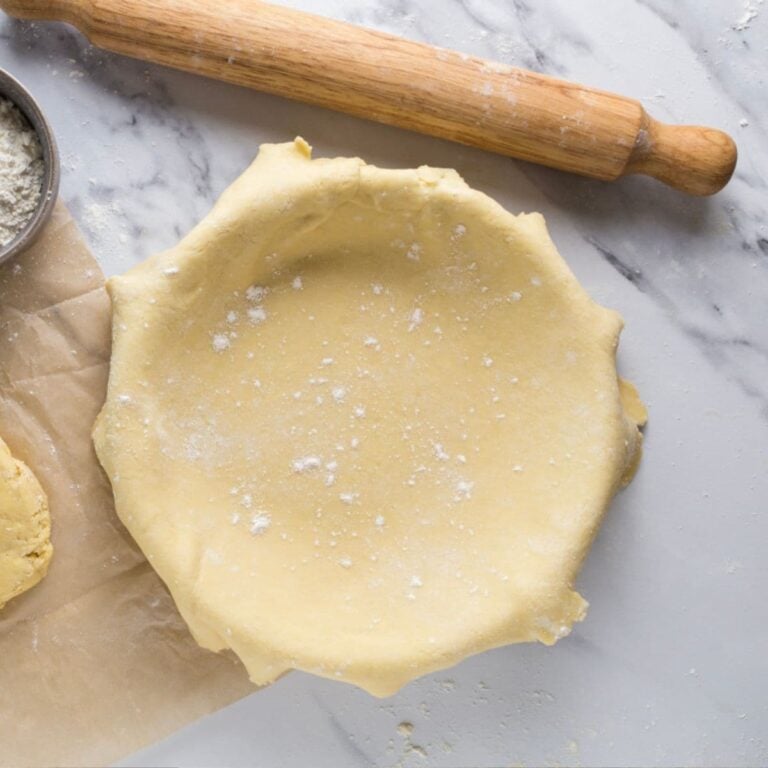 Rolled sourdough pie crust fitted into a pie dish with extra dough and flour nearby.