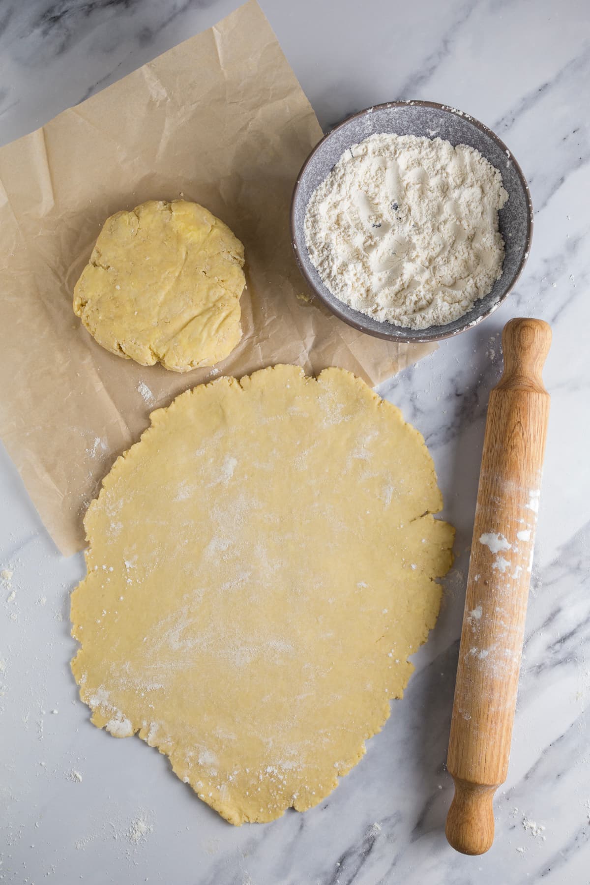 Sourdough pie crust dough rolled thin on a floured countertop beside a rolling pin and bowl of flour.