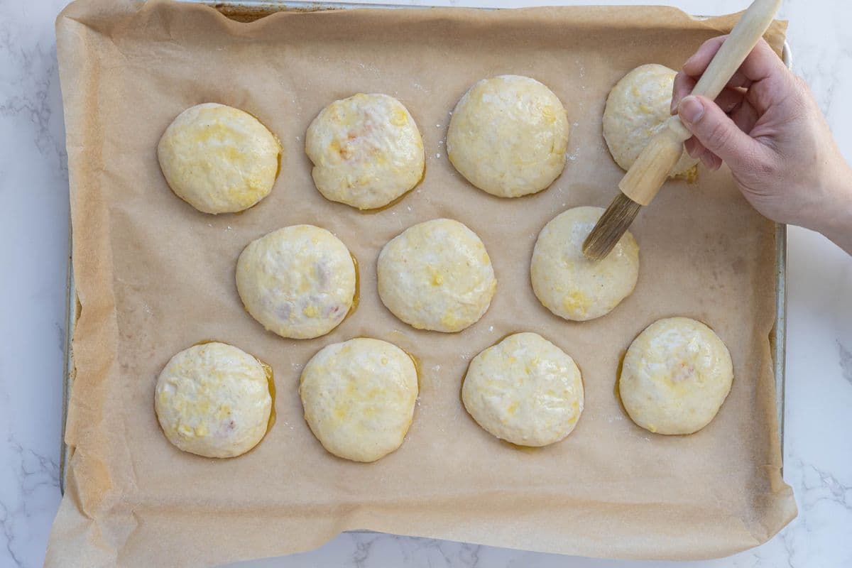 Brushing garlic butter over shaped sourdough pizza pockets before baking for a golden crust.