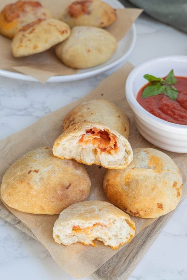 Golden brown sourdough pizza pockets with a soft crust and cheesy pepperoni filling served on a piece of parchment paper with pizza sauce.