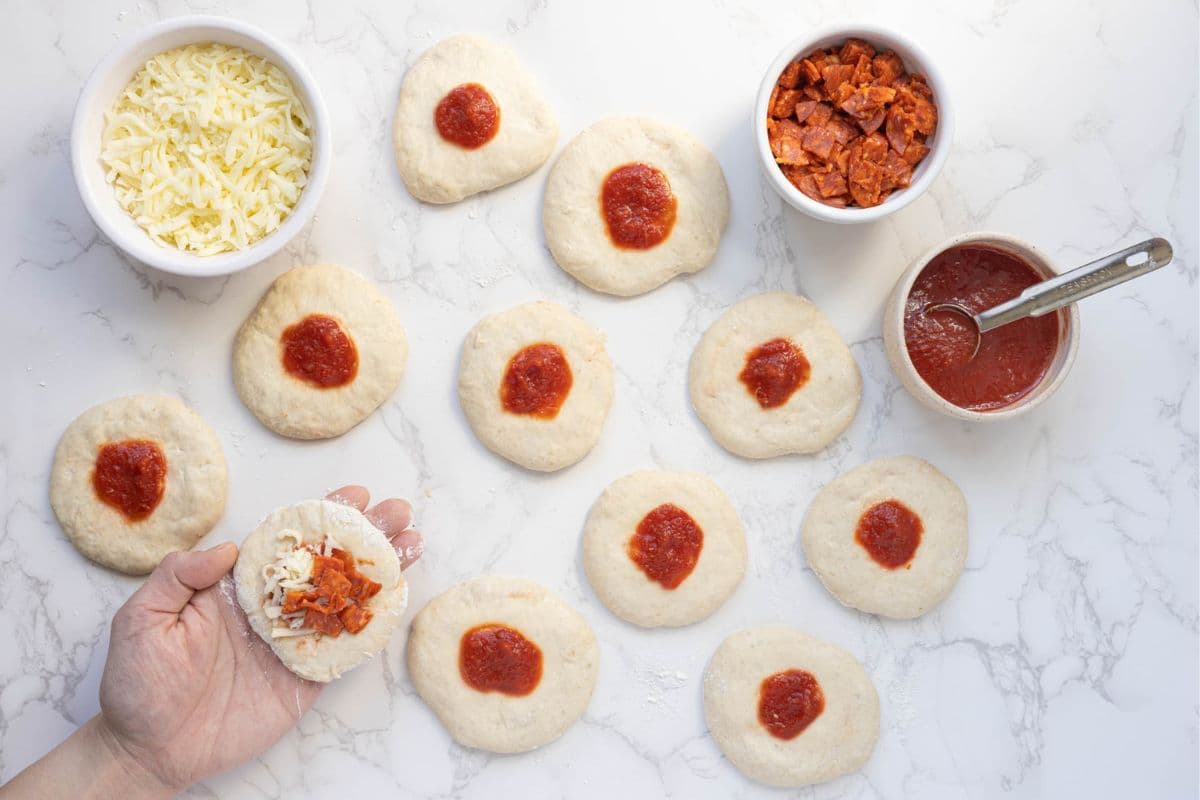 Hand filling sourdough pizza dough rounds with mozzarella cheese and chopped pepperoni before sealing.