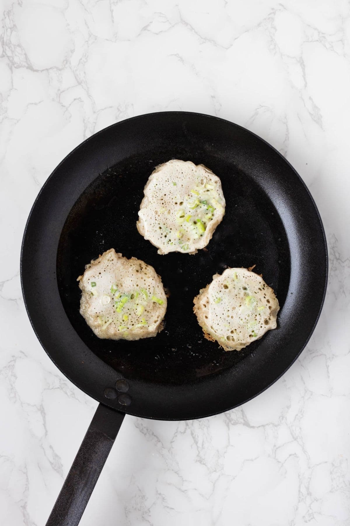 Scallion pancake batter cooking in a skillet with sliced green onions visible in the batter.