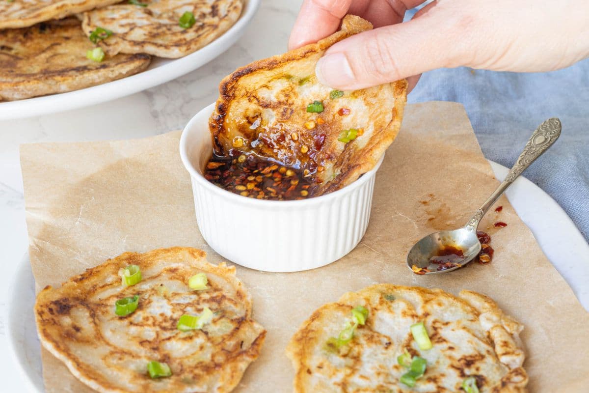 Hand dipping a crispy sourdough scallion pancake into a savory chili dipping sauce.