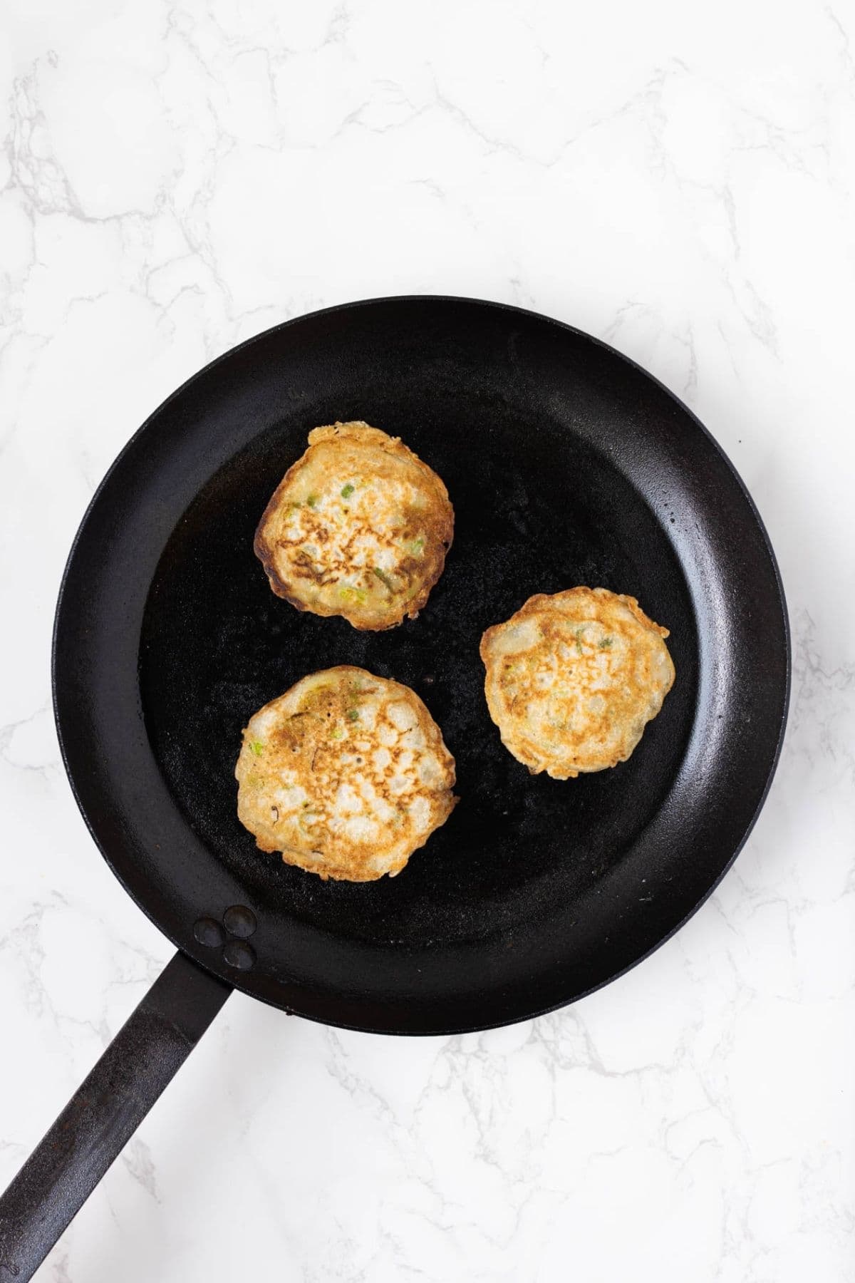 Sourdough scallion pancakes cooking in a skillet until golden brown and crispy.