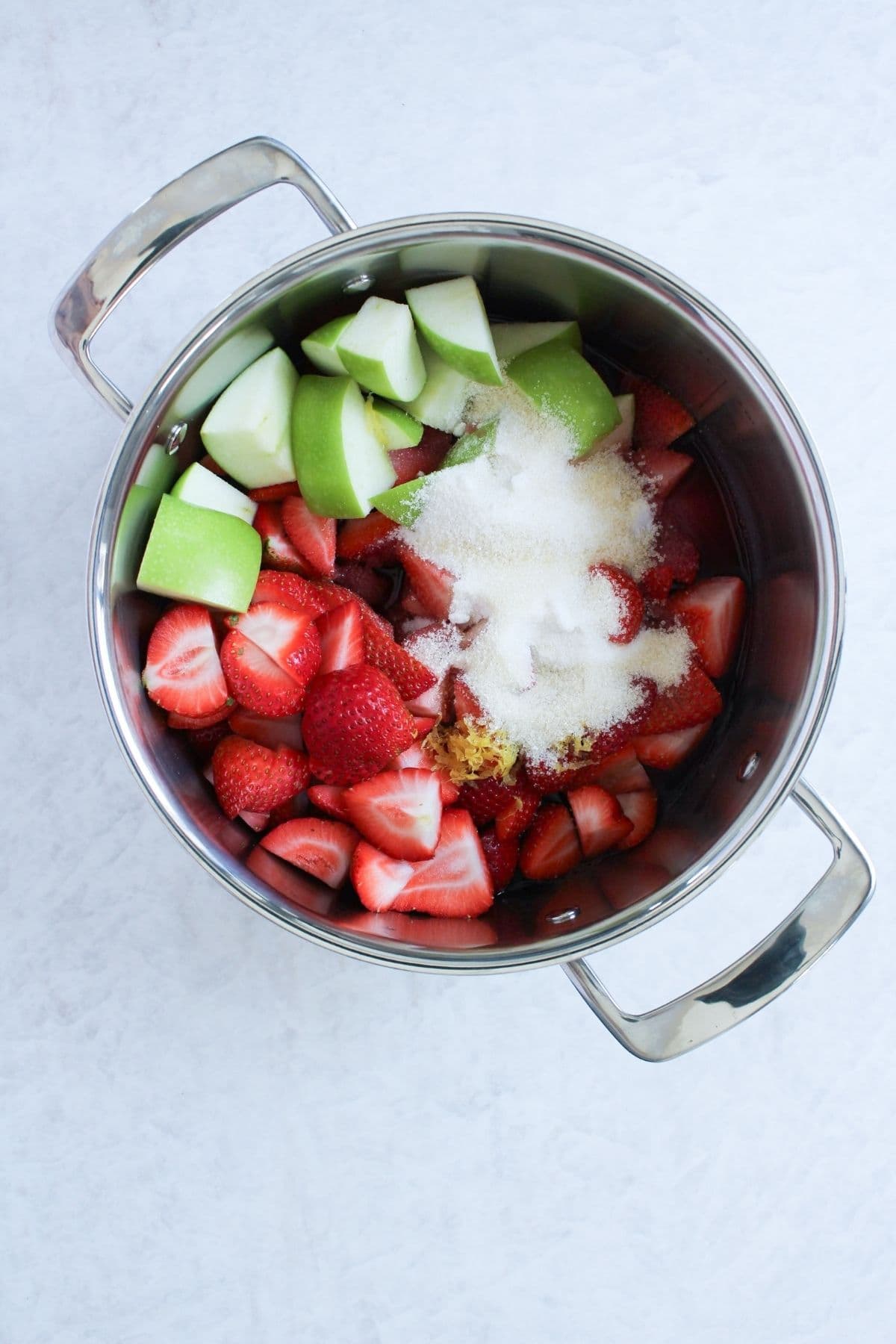 Fresh strawberries, diced green apple, sugar, lemon zest and juice, and pomegranate juice combined in a pot to make strawberry pomegranate jam.