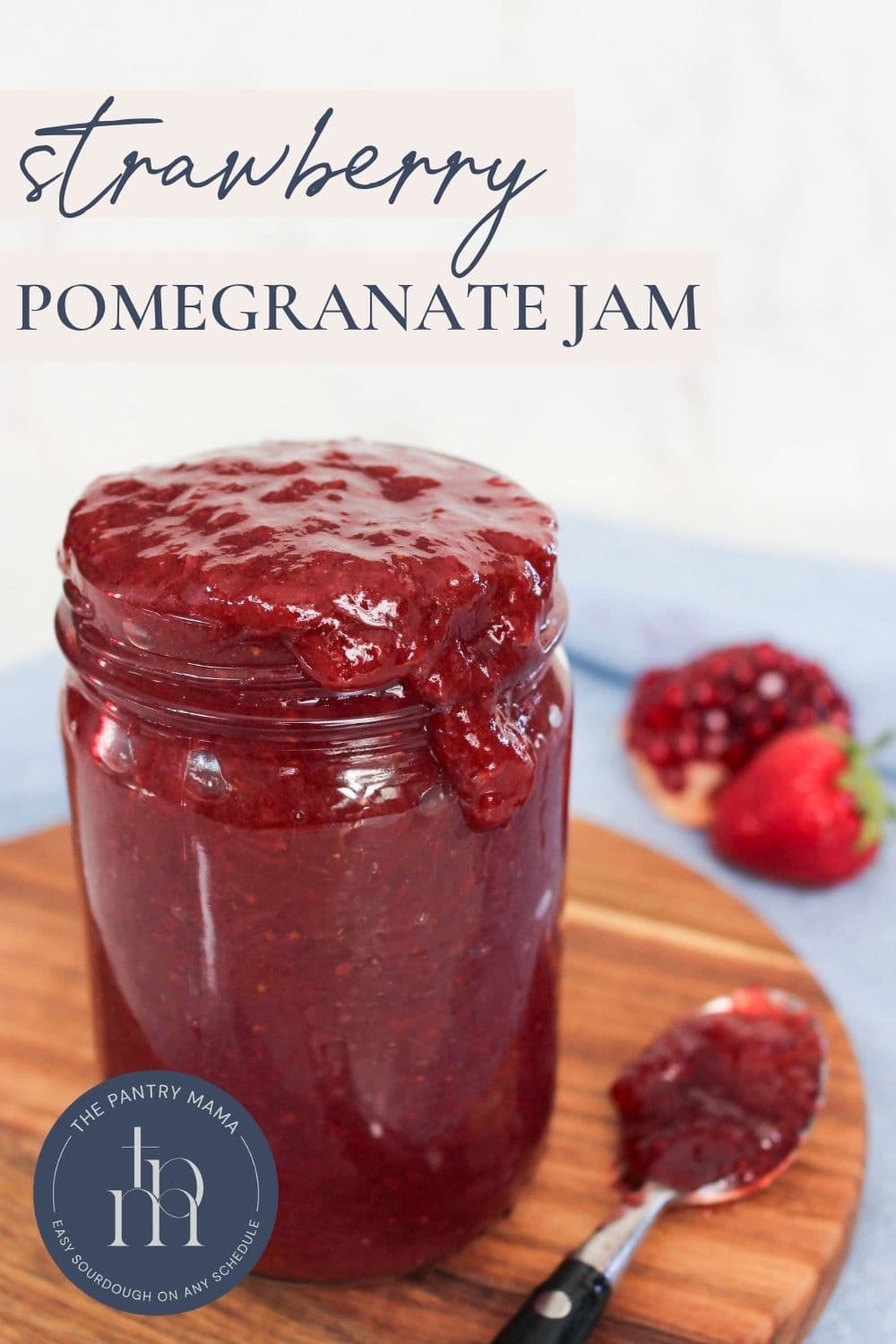 Homemade strawberry pomegranate jam in a glass jar on a wooden board with text overlay for a Pinterest Pin image.