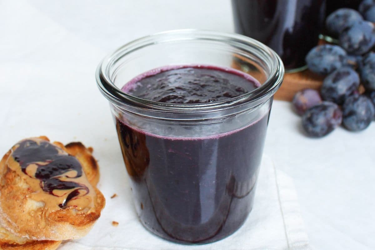 Jar of homemade grape jelly served beside fresh grapes and peanut butter toast.