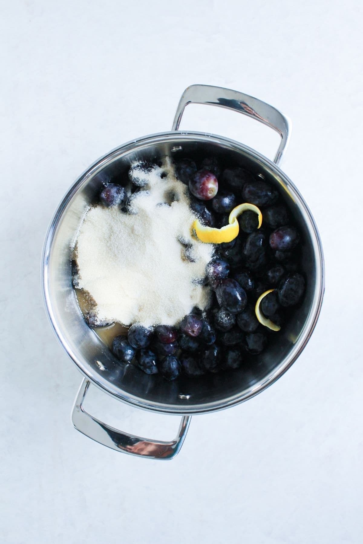 Fresh grapes, sugar, water, and lemon peel combined in a saucepan before cooking.