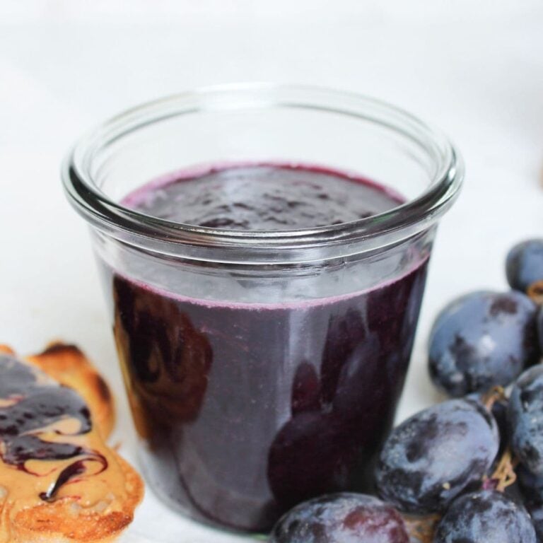 Jar of homemade grape jelly beside fresh grapes and peanut butter toast spread with grape jelly.