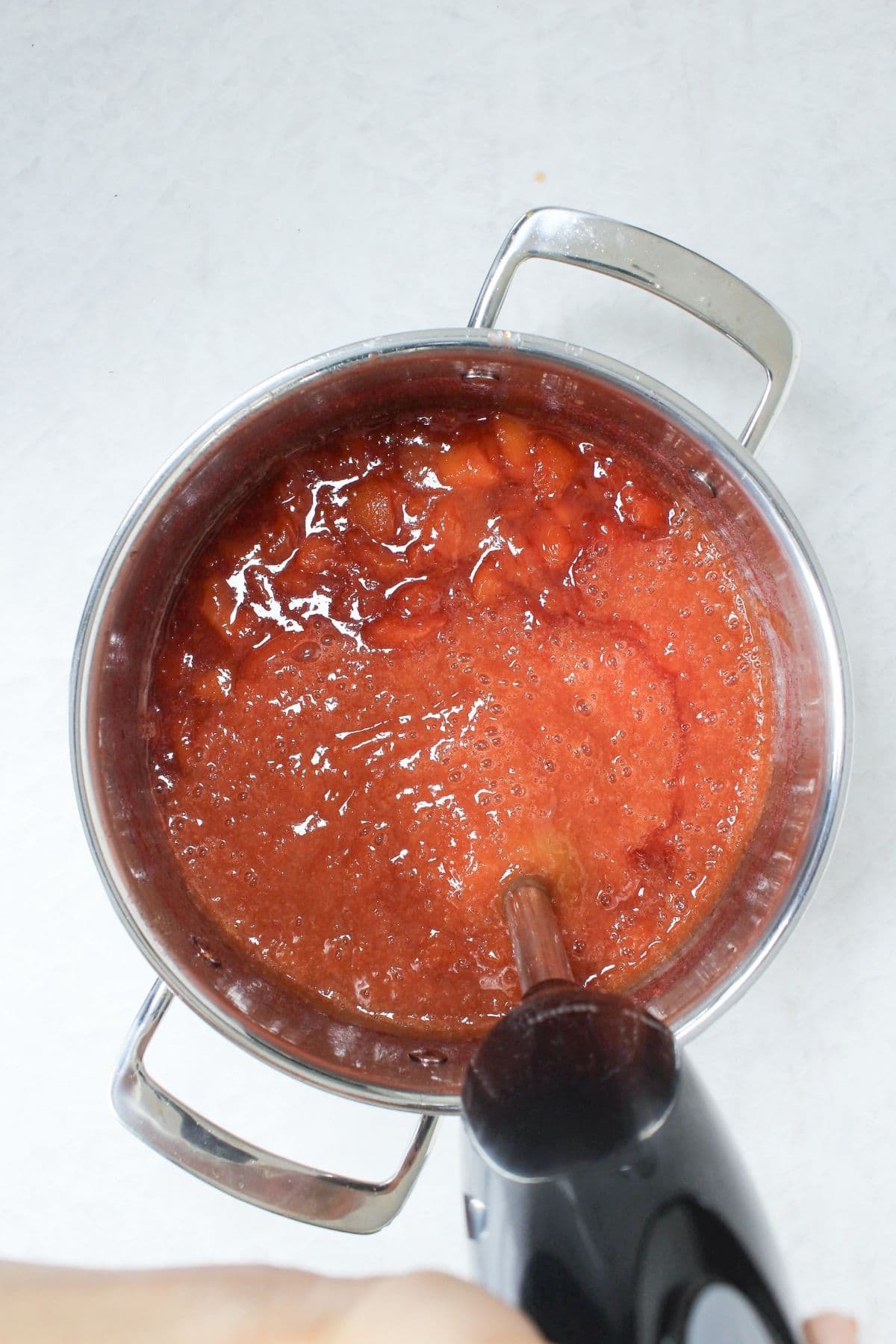 Using an immersion blender to blend cooked peaches into smooth peach vanilla bourbon jam.