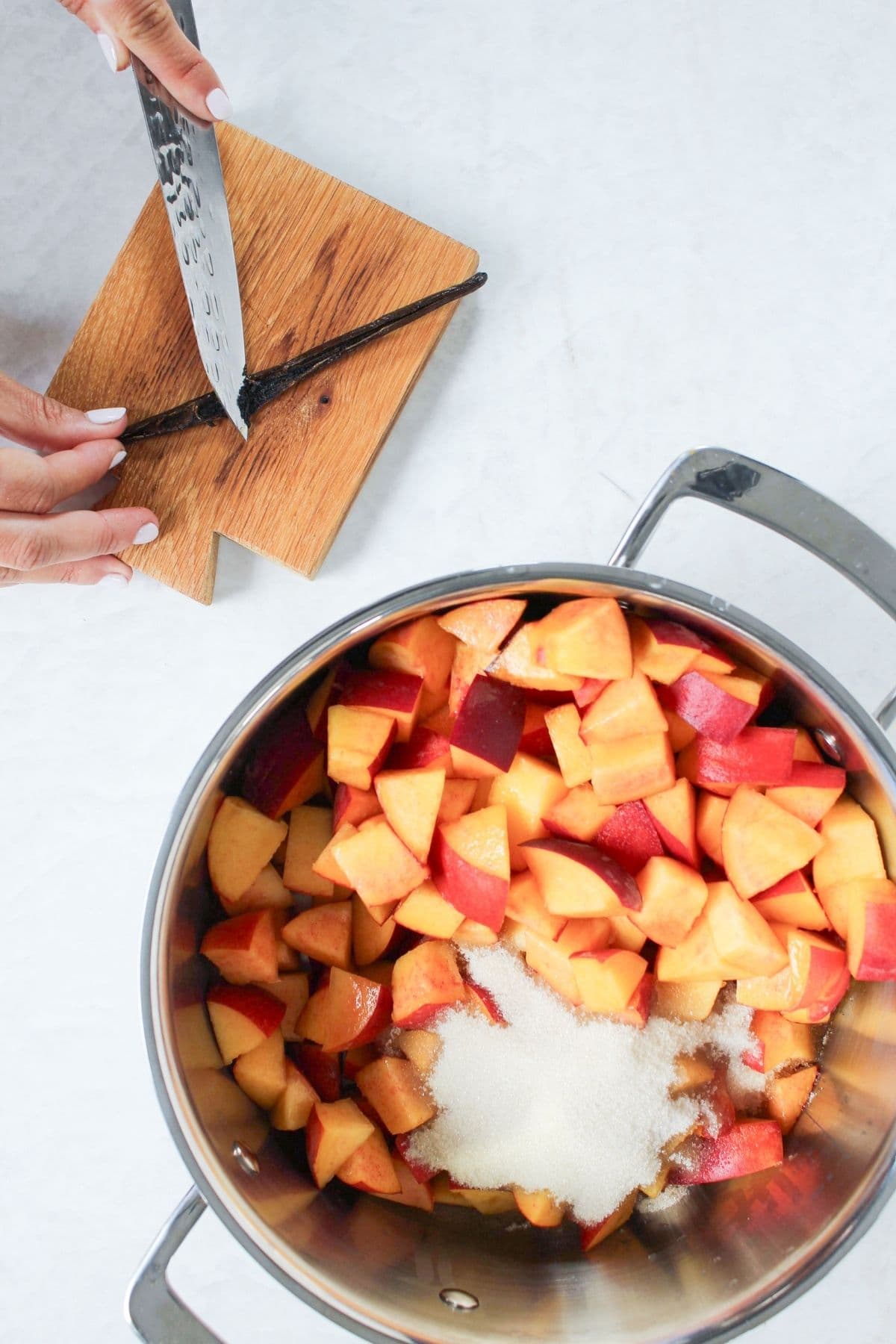 Chopped fresh peaches, sugar, and a vanilla bean being added to a pot to make peach vanilla bourbon jam.