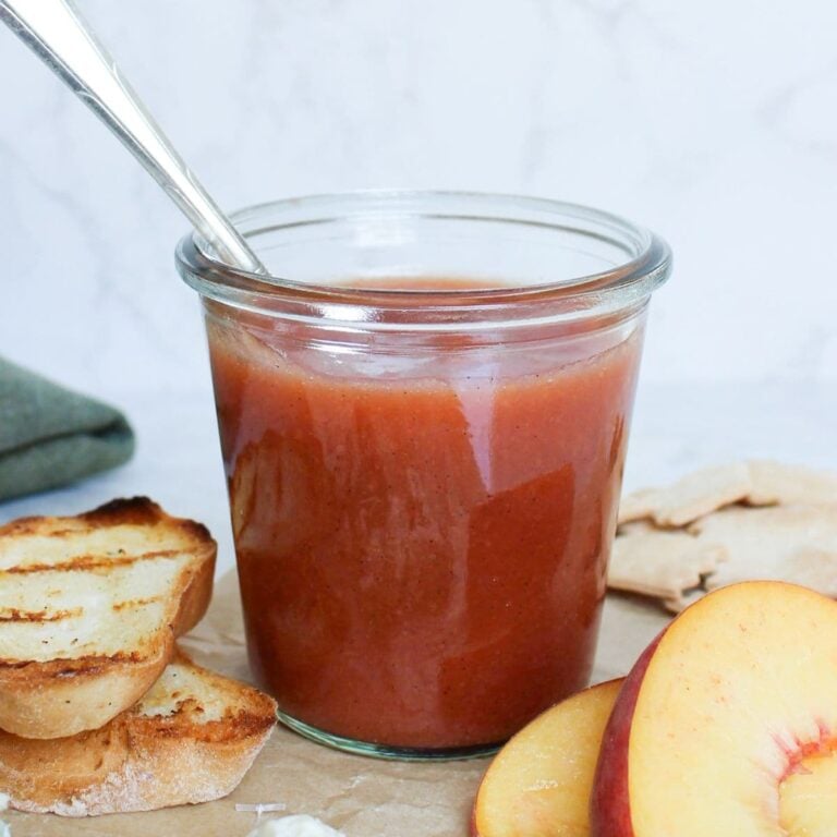 Homemade peach vanilla bourbon jam in a glass jar with grilled bread, fresh peaches, crackers, and blue cheese.