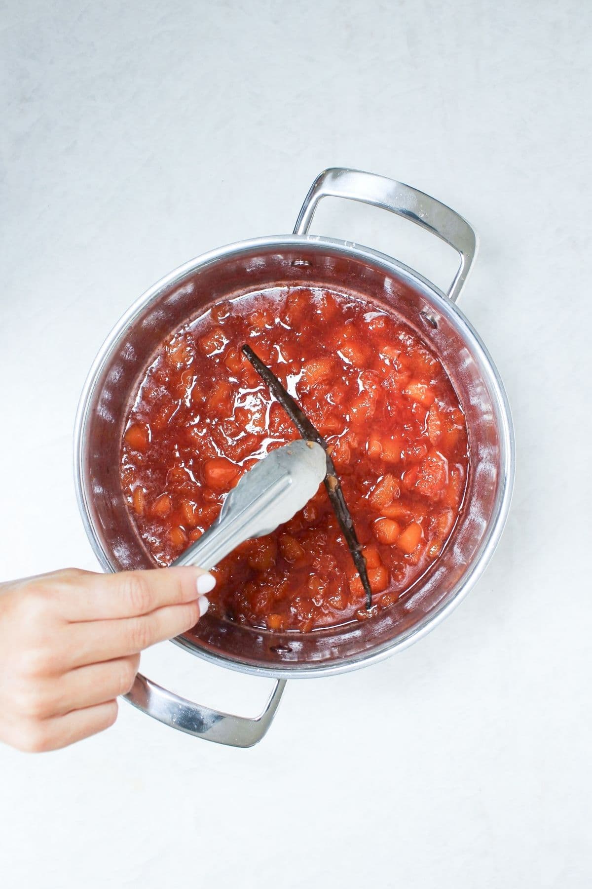Removing the vanilla bean pod from simmering peach vanilla bourbon jam before blending.