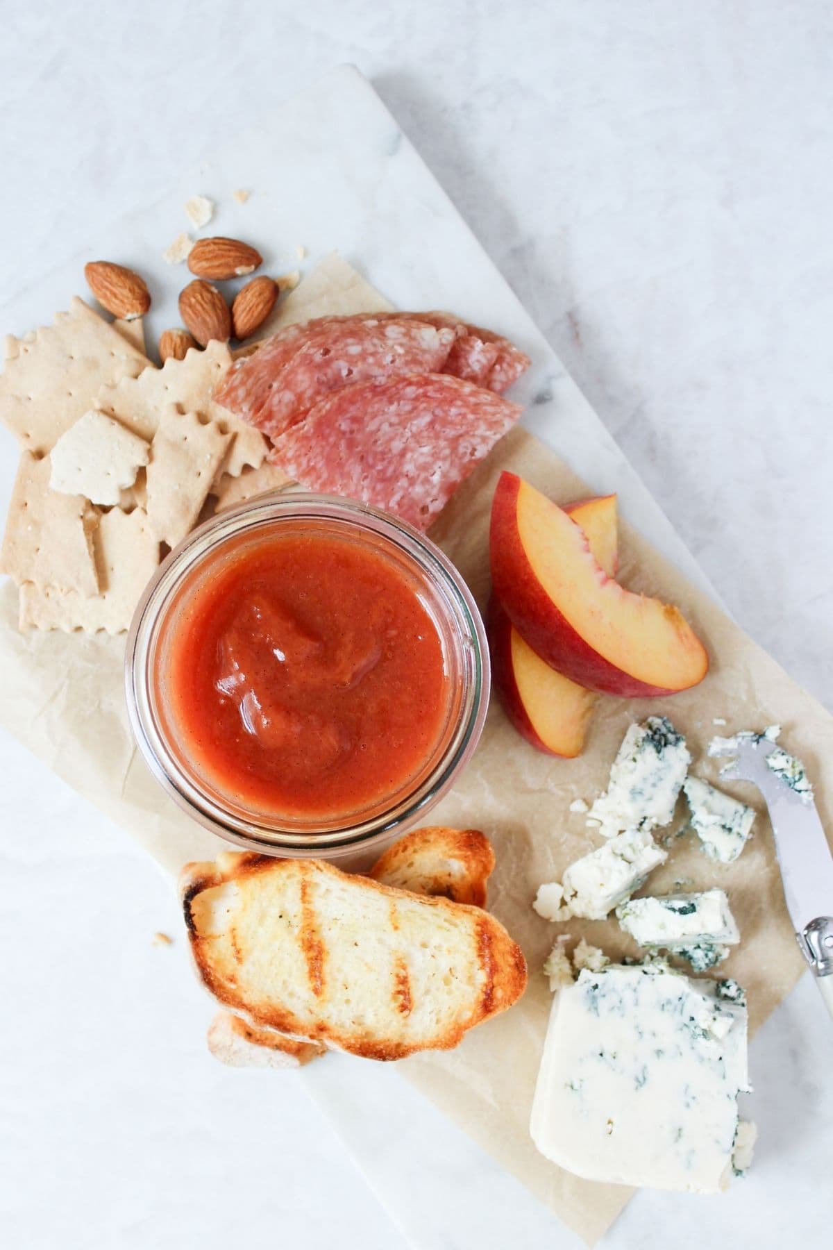 Peach vanilla bourbon jam served on a cheeseboard with blue cheese, salami, sourdough crackers, toasted sourdough bread, almonds, and fresh peaches.