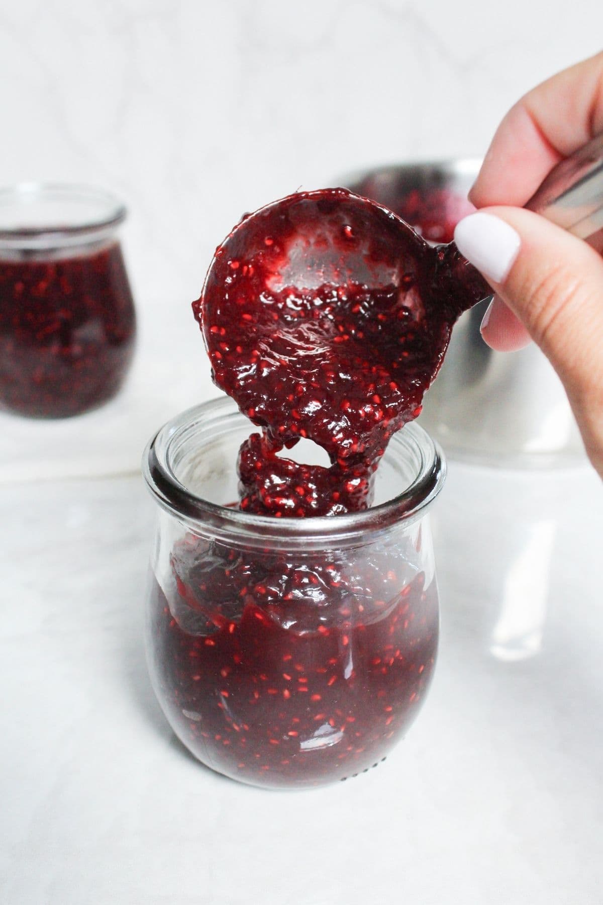 Close-up of thick homemade chocolate raspberry jam being spooned into a glass jar.