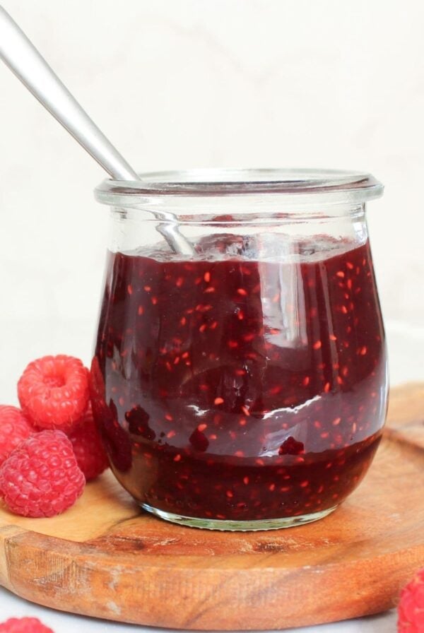 Close-up of homemade chocolate raspberry jam in a glass jar with a spoon and fresh raspberries.